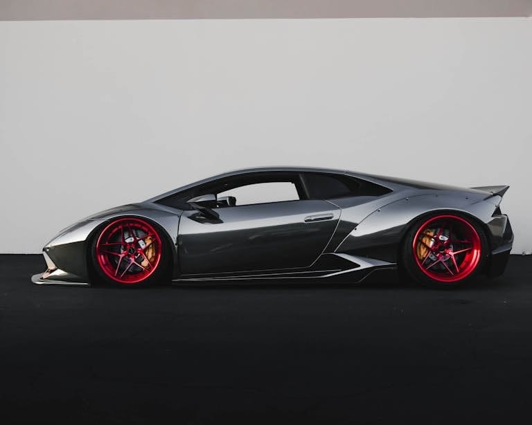Grey Lamborghini sports car with distinctive red rims parked outdoors.